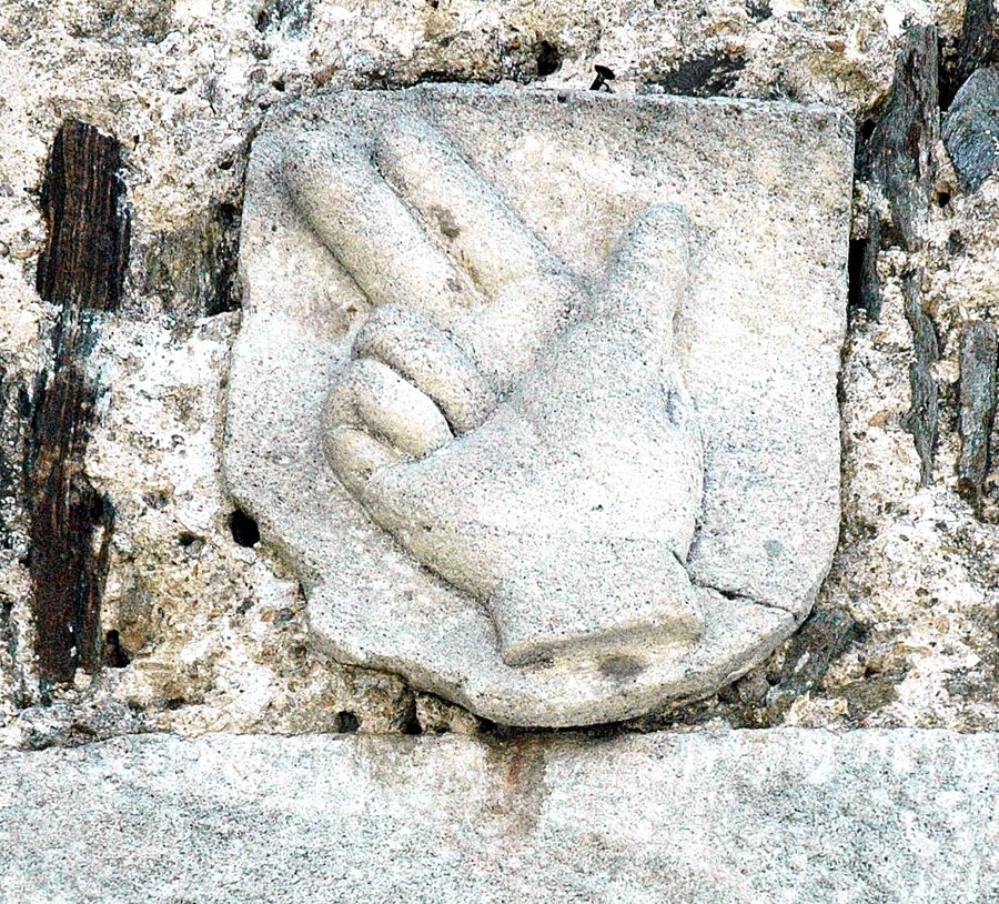 Steinrelief einer Schwurhand: zwei erhobene Finger in einem Wappenschild über einem Portal